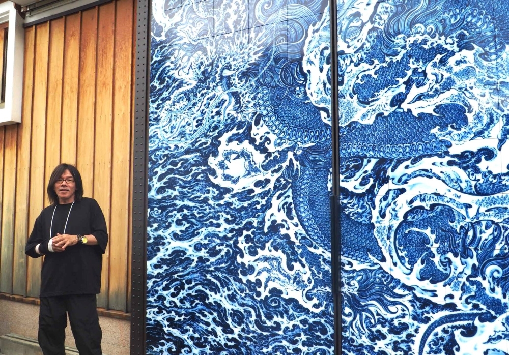 Yuki Hayama tells visitors about his dragon mural, an enlarged print of his ceramic work, showcased on the doors of the Masuda Sake Brewery.