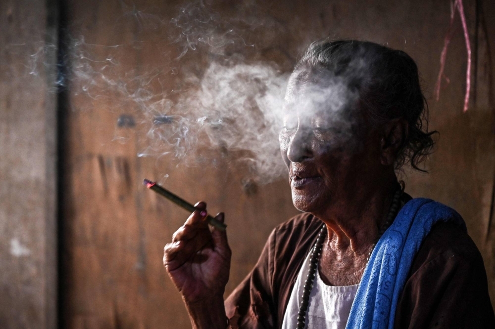 Dar San Ye smoking in her home in Yangon. Forty years ago, she stood in a river squaring up to a North Korean agent on the run after a botched assassination, a live grenade primed in his hand. 