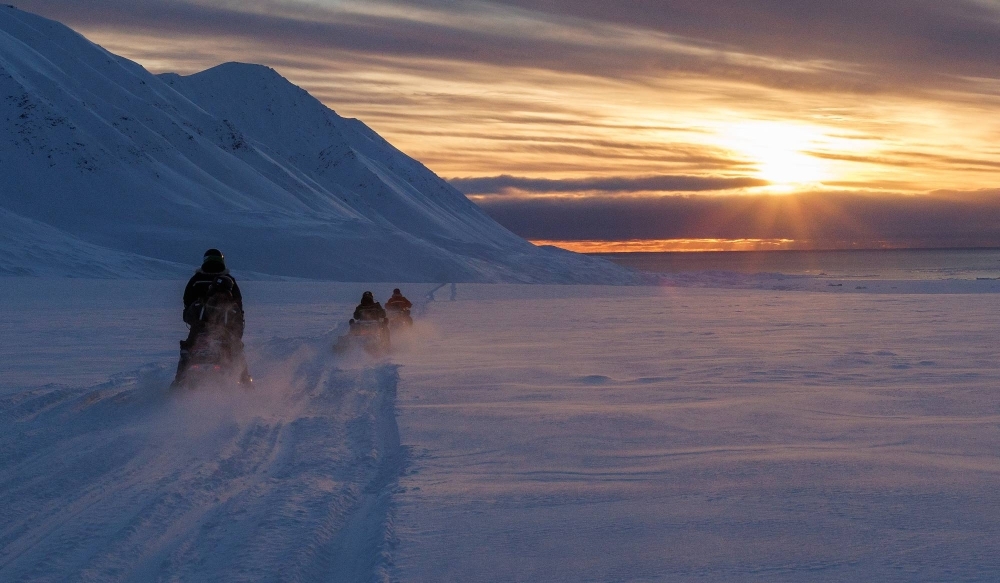 Scientists drive their snowmobiles across the arctic.