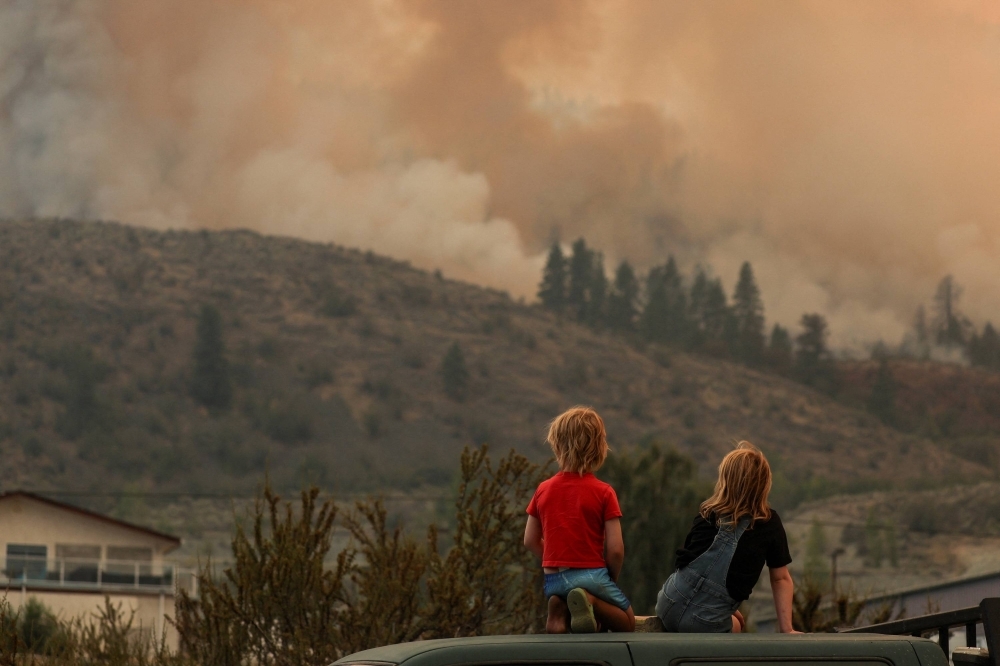 Locals gather to watch firefighting efforts amid heavy smoke from the Eagle Bluff wildfire, after it crossed the Canada-U.S. border from the state of Washington and prompted evacuation orders, in Osoyoos, British Columbia, Canada