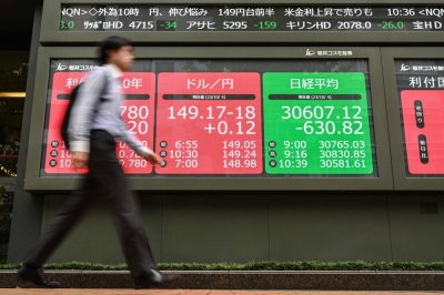 A pedestrian walks past an electronic signboard showing data from the Tokyo Stock Exchange and on the Japanese yen after the currency rebounded slightly after hitting ¥150 to the U.S. dollar in overnight trading, along a street in central Tokyo on Oct. 4.