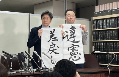 Lawyers Kazuyuki Minami (left) and Masafumi Yoshida (right) representing a transgender woman show off signs that say "unconstitutional" and "sent back" to a lower court, during a news conference Wednesday in Tokyo after a Supreme Court decision.