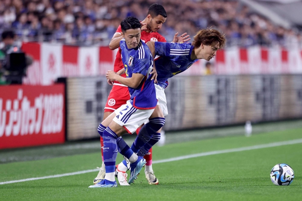 Ko Itakura (right) and Yukinari Sugawara fight for the ball with Tunisia's Elies Ashley during an international friendly football match between Japan and Tunisia in Kobe on Oct. 17.