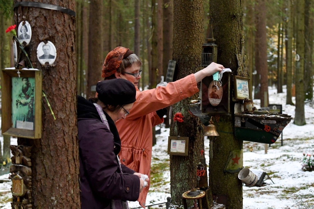 A woman cleans a portrait displayed on a tree to mark the Day of Victims of Political Repressions, who were buried during the Stalin era in the woods on the outskirts of St. Petersburg on Monday.