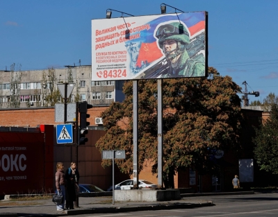 People stand next to a board promoting military service in Donetsk, Russian-controlled Ukraine, on Oct. 11. A Brooklyn man and a Montreal couple have been charged with attempting to smuggle tech to Russia to support the Kremlin's invasion of Ukraine.