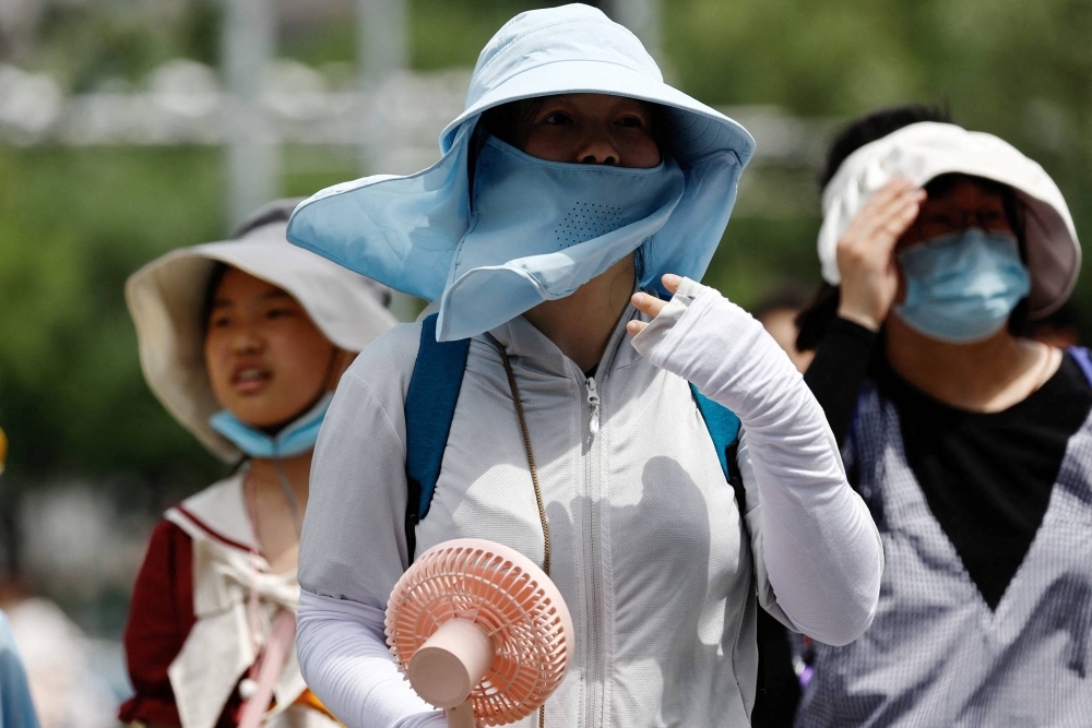 People wearing sun protection gear amid a heat wave walk on a street in Beijing in July. 