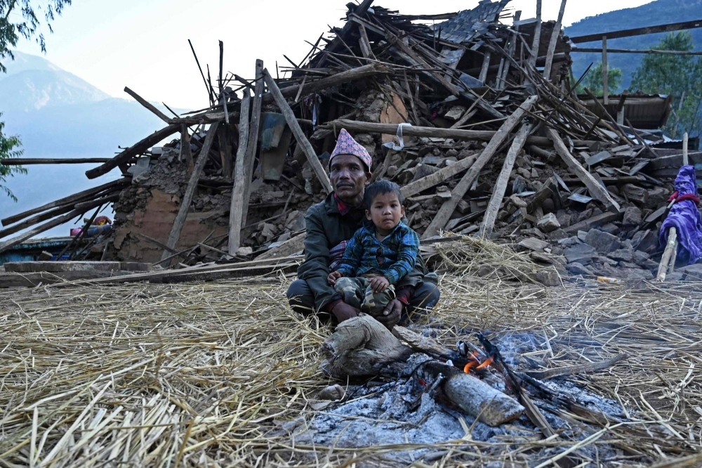 Survivors of a recent earthquake sit in front of a damaged house in Chiuri village at Jajarkot district on Sunday. 