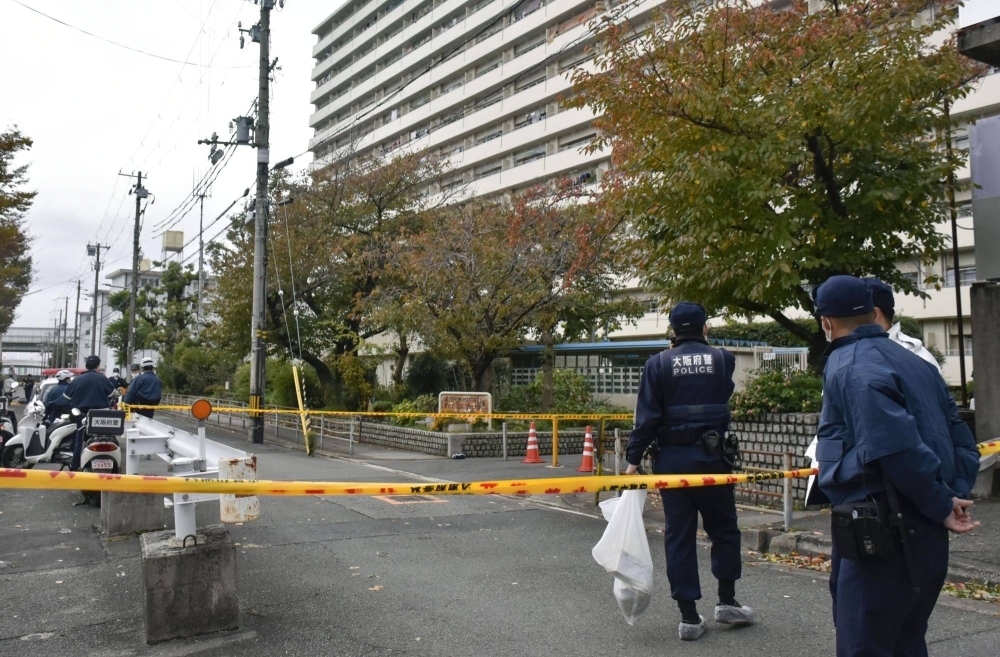 Police examine the area near an apartment complex in Osaka where a woman was injured and a knife-carrying man was shot by an officer on Monday.