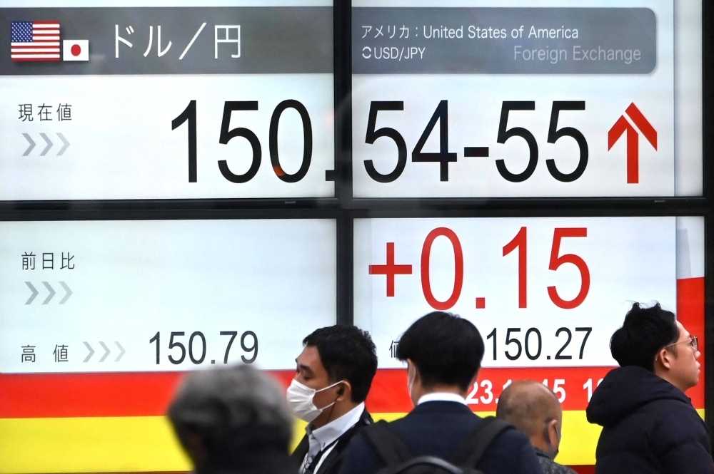 People pass an electronic board showing the rate of the yen against the dollar on a street in Tokyo on Wednesday.