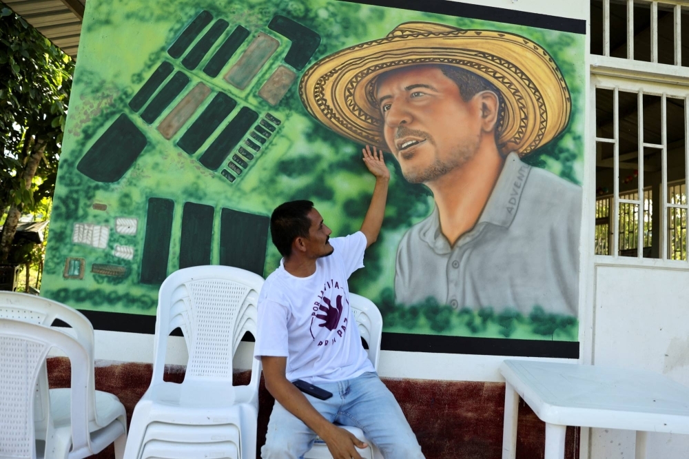 Armando Aroca, environmentalist, former guerrilla and current nursery manager of the Common Community Multi Active Cooperative (COMUCCOM) farm, points to a mural with the image of murdered environmentalist Jorge Santofimio in Puerto Guzman, Colombia, on June 27.