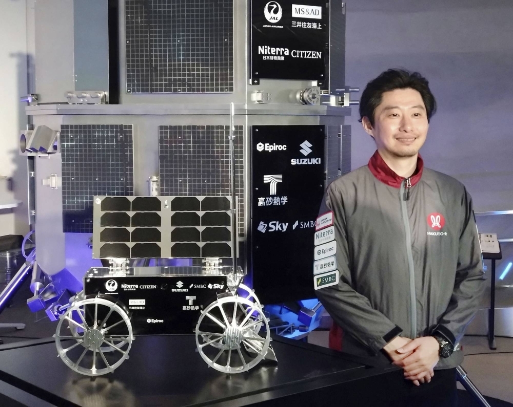 Japanese startup Ispace CEO Takeshi Hakamada poses next to the firm's moon rover on Thursday in Tokyo.