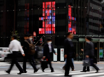 Pedestrians walk past an electronic board displaying various companies' share prices, in a business district in Tokyo on Oct. 31.