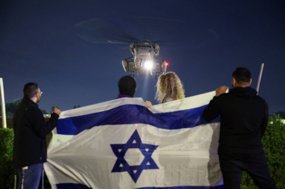 People hold an Israeli flag as a helicopter carrying released hostages arrives at Sheba Medical Center in Ramat Gan, in Tel Aviv, on Tuesday.