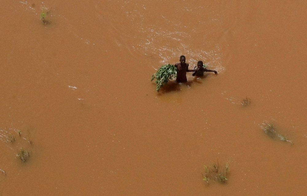 People hold on to plants as they wade through flood waters after they were displaced following heavy rains in Garsen, Tana Delta within Tana River county, Kenya, on Nov. 23.