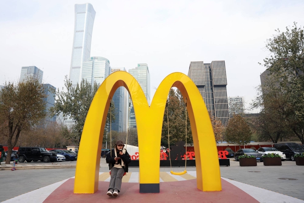 A woman sits on a swing attached to a giant McDonald's sign outside its themed exhibition in Beijing on Monday.