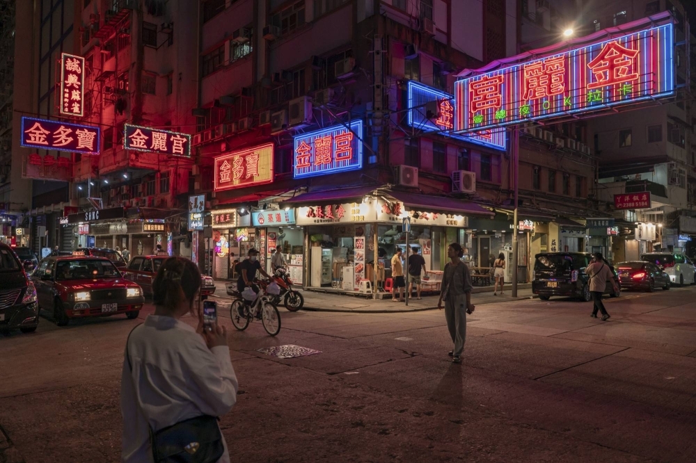A tourist poses for a photograph under signs for karaoke nightclubs in the Mong Kok district of Hong Kong. The government crackdown on neon signs stems from safety and environmental concerns, but the campaign evokes the fading of the city itself.