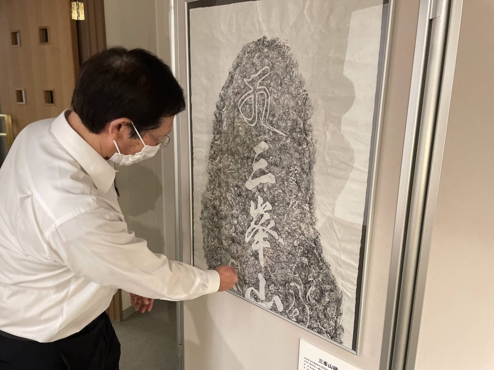 Shinichiro Ishiguro, the director of a folk museum in Murata, Miyagi Prefecture, shows a rubbed, inked copy of a stone slab with the inscription “Mitsumine-san” (Mount Mitsumine) during an exhibition he curated recently. 