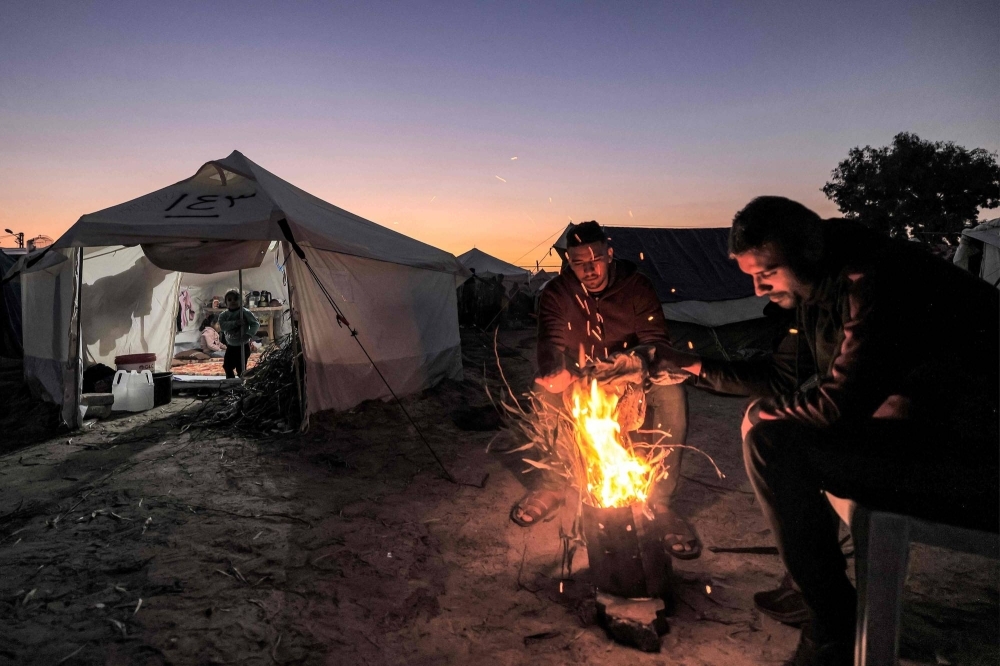 Men warm up around a fire outside one of the tents housing Palestinians displaced by the conflict in Gaza on Monday.