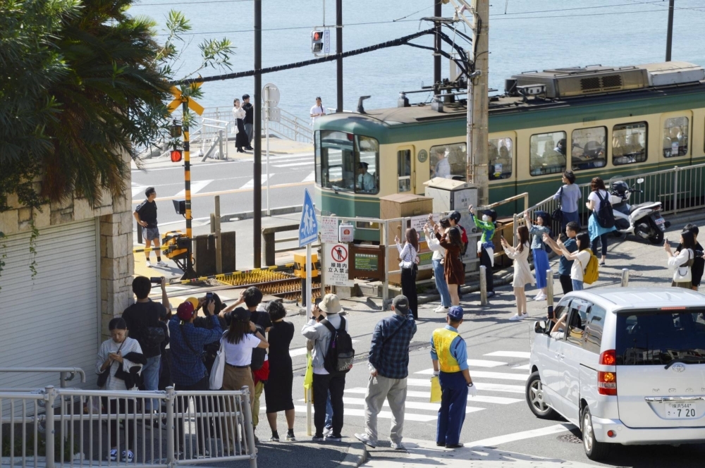 Foreign tourists take pictures of an Enoshima Electric Railway train near a railroad crossing in Kamakura, Kanagawa Prefecture, in October.