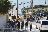 Foreign tourists take pictures of an Enoshima Electric Railway train near a railroad crossing in Kamakura, Kanagawa Prefecture, in October. | Kyodo