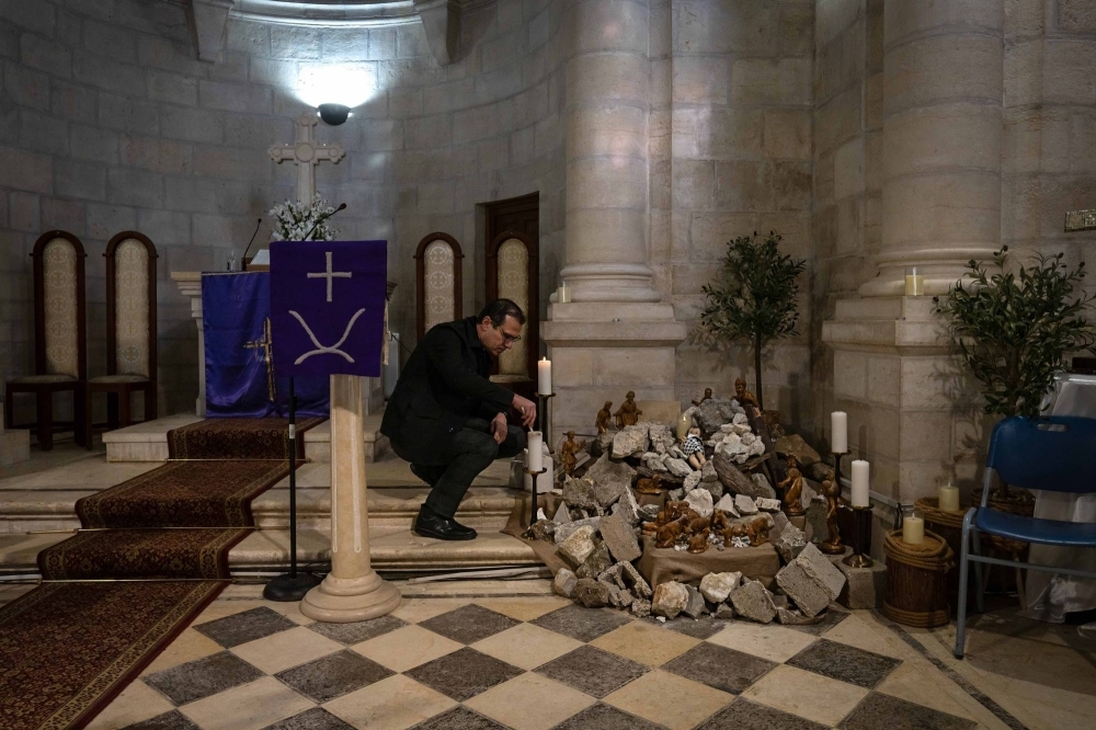 The Rev. Munther Isaac lights a candle next to an improvised crèche in Bethlehem on Dec. 13. The baby Jesus is lying not in a makeshift cradle of hay and wood, but among the rubble of broken bricks, stones and tiles that represent Gaza’s destruction.