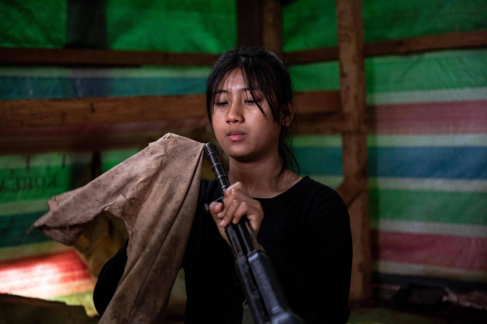 A female member of the Mandalay People's Defense Forces repairs and cleans a weapon at their base camp in the forest near Namhsan Township in Myanmar's northern Shan State. In the hills of northern Myanmar young women fly combat drones, treat wounded comrades and patrol the front lines — new roles in the battle to overthrow the military junta.