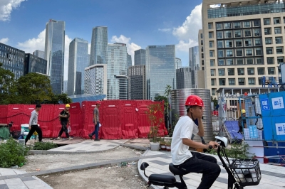 Workers walk past an underconstruction area with completed office towers in the background in Shenzhen's Qianhai new district on Aug. 25, 2023.