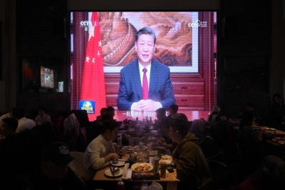 People have their dinner at a restaurant as a screen broadcasts Chinese leader Xi Jinping's New Year's speech in Beijing on Sunday.