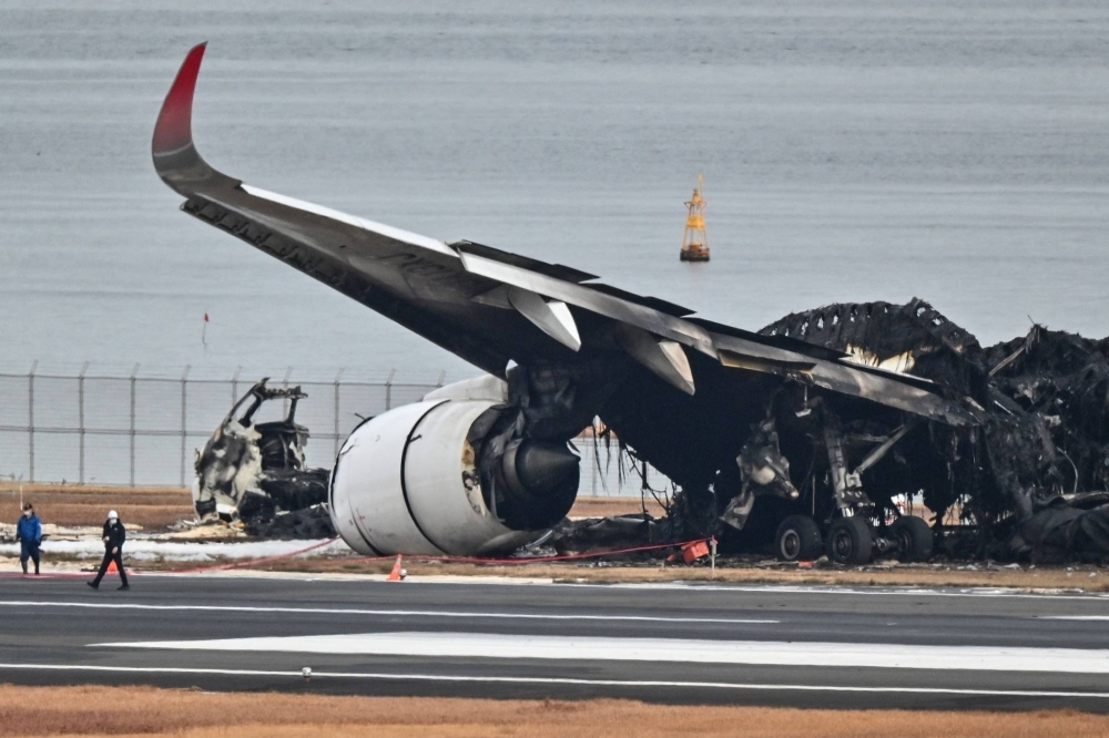 Officials examine the burned wreckage of a Japan Airlines passenger plane on the tarmac at Haneda Airport in Tokyo on Wednesday.