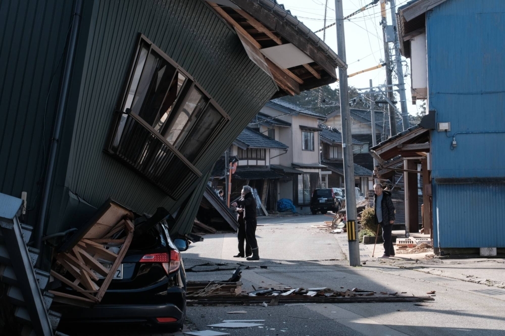 A damaged vehicle under a collapsed house following an earthquake in Nanao, Ishikawa Prefecture, on Tuesday. Speculation that the Bank of Japan might shift its policy this month is receding, as the central bank has to assess the adverse impact from the Noto Peninsula disaster on the economy.