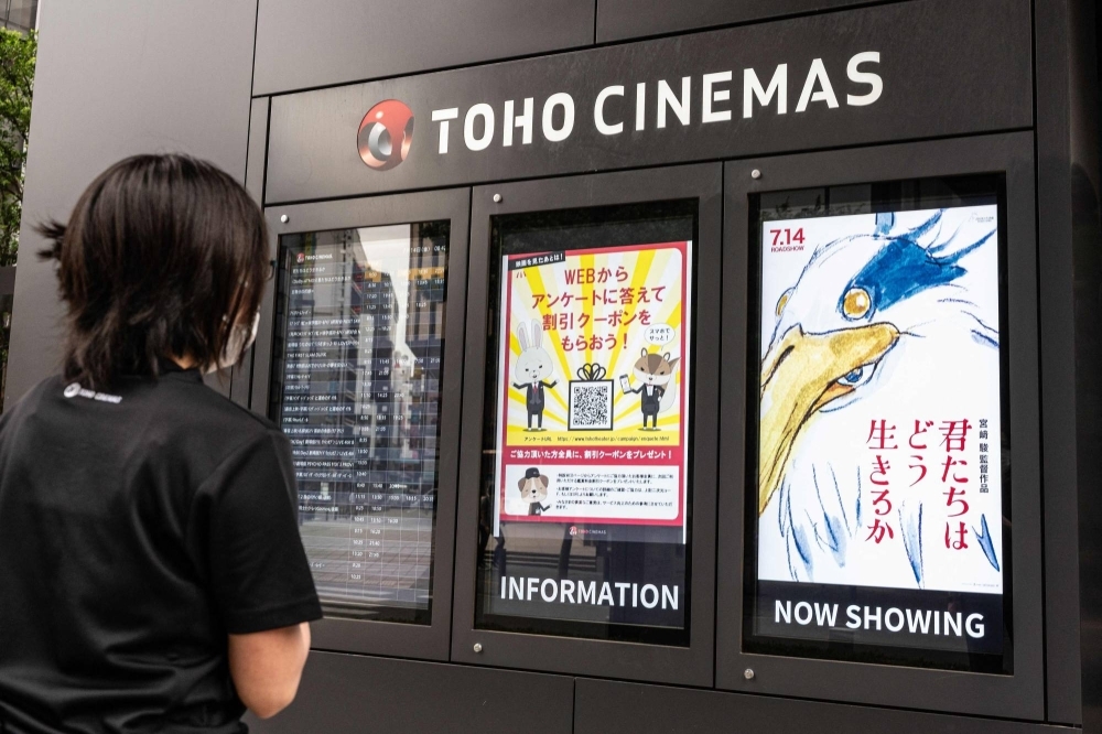 A cinema employee checks a display showing a digital poster (right) for Hayao Miyazaki's most recent film, "The Boy and the Heron," in Tokyo on July 14.
