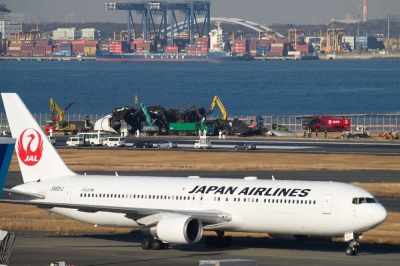 A Japan Airlines aircraft taxis past the wreckage of the company's passenger jet that collided with a Japan Coast Guard plane on Jan. 2, at Haneda Airport in Tokyo on Friday.