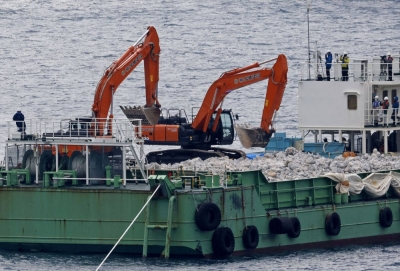 Heavy machinery is used to pour in stone material from a work boat into the sea off the coast of Nago, Okinawa Prefecture.