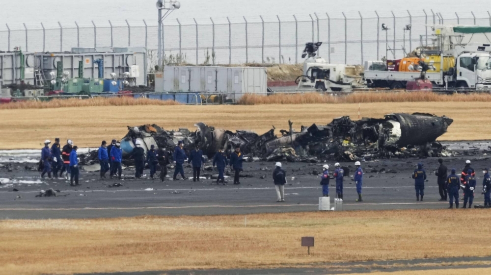 Police investigators and firefighters examine a burnt-out Japan Coast Guard aircraft on a runway at Tokyo's Haneda airport on Jan. 3, the day after its deadly collision with a Japan Airlines jetliner.