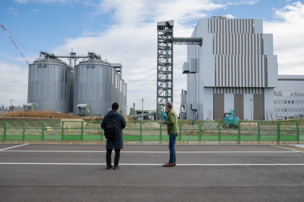 Ben Parfitt (right) stand outside Renova’s Sendai Gamo Biomass power plant. The round tanks on the left are for storing biomass fuel.