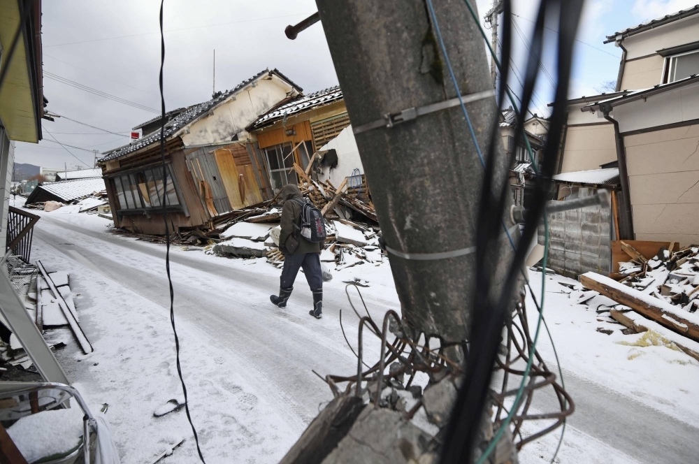 A person walks amid the snowy wreckage of collapsed homes and power lines in earthquake-hit Wajima, Ishikawa Prefecture, on Tuesday.