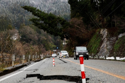 Cars drive past a damaged road, in the aftermath of an earthquake, in Wajima, Ishikawa Prefecture.