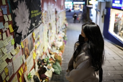 A woman prays while reading condolence messages attached to the wall of a narrow alley of Itaewon, where the deadly Halloween crush that killed more than 150 in October happened, in Seoul, in December 2022.