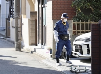 A police officer examines the area around a house in Tokyo's Adachi Ward on Friday after the bodies of a couple with stab wounds were found in the house. | Kyodo