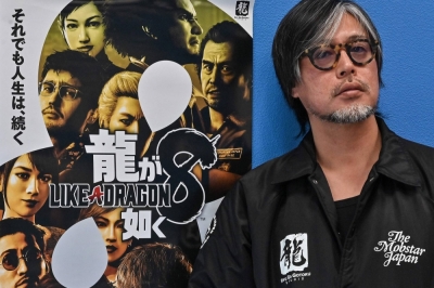 Executive officer, producer and director Masayoshi Yokoyama poses next to a promotional poster for Like a Dragon: Infinite Wealth. The Yakuza gangster series has long been seen as a Japanese version of Grand Theft Auto, but Yokoyama dismisses any such comparison. 