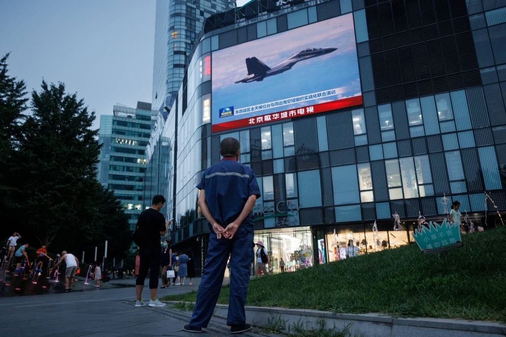 A man watches a news broadcast showing a fighter jet during joint military operations near Taiwan by the Chinese People's Liberation Army, at a shopping center in Beijing in August 2022. 