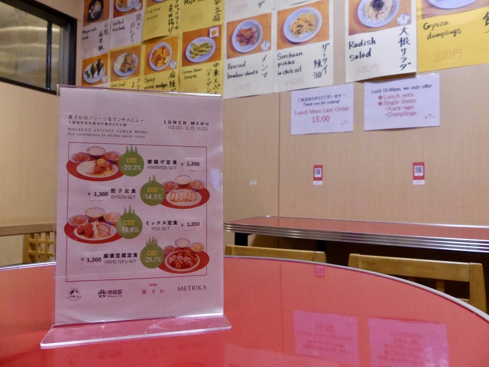A menu at Masaka, a vegan restaurant in Tokyo’s Shibuya Ward, shows the rate of carbon dioxide emissions cuts for dishes compared with meat-based alternatives.
