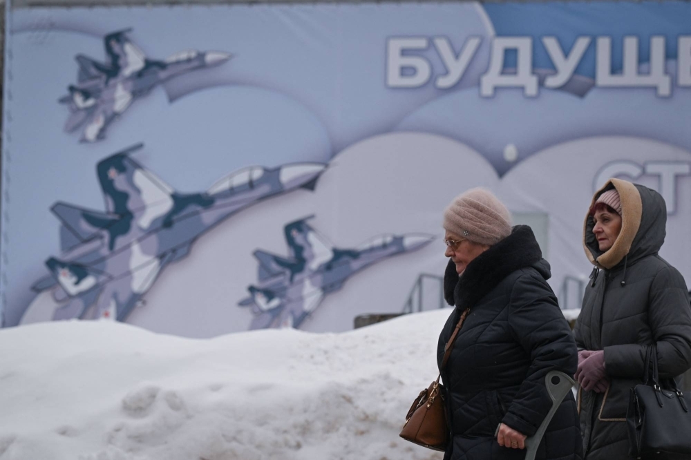 Women walk past an army-related billboard at the All-Russia Exhibition Center in Moscow on Jan. 24.