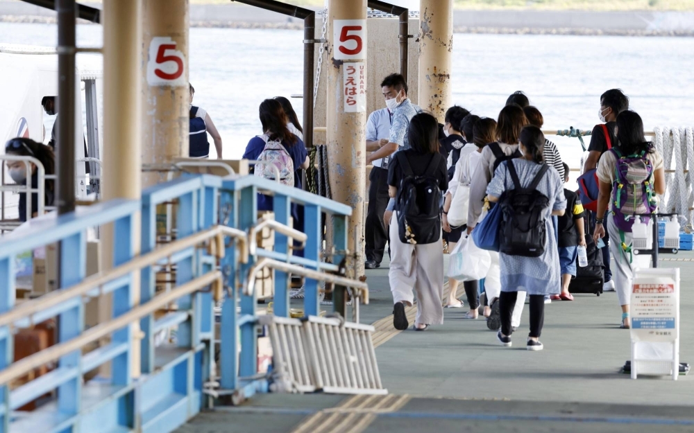 Tourists board a ferry to Iriomote Island, Okinawa Prefecture, from Ishigaki, another island in the prefecture. The local government of the town of Taketomi, which includes Iriomote Island, is planning to introduce a visitor's tax to fund environmental protection measures in the face of rising tourist numbers.