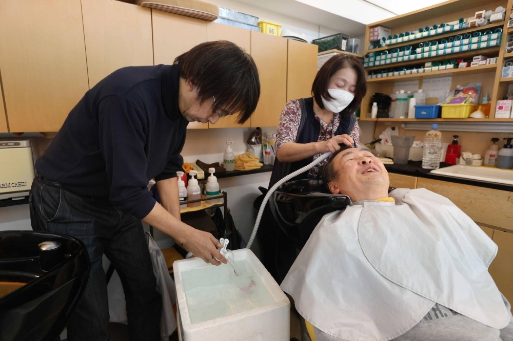 Noboru Ito (left) uses well water for a makeshift shower at his Real Hair Cutting You beauty salon in Nanao, Ishikawa Prefecture, on Jan. 24.