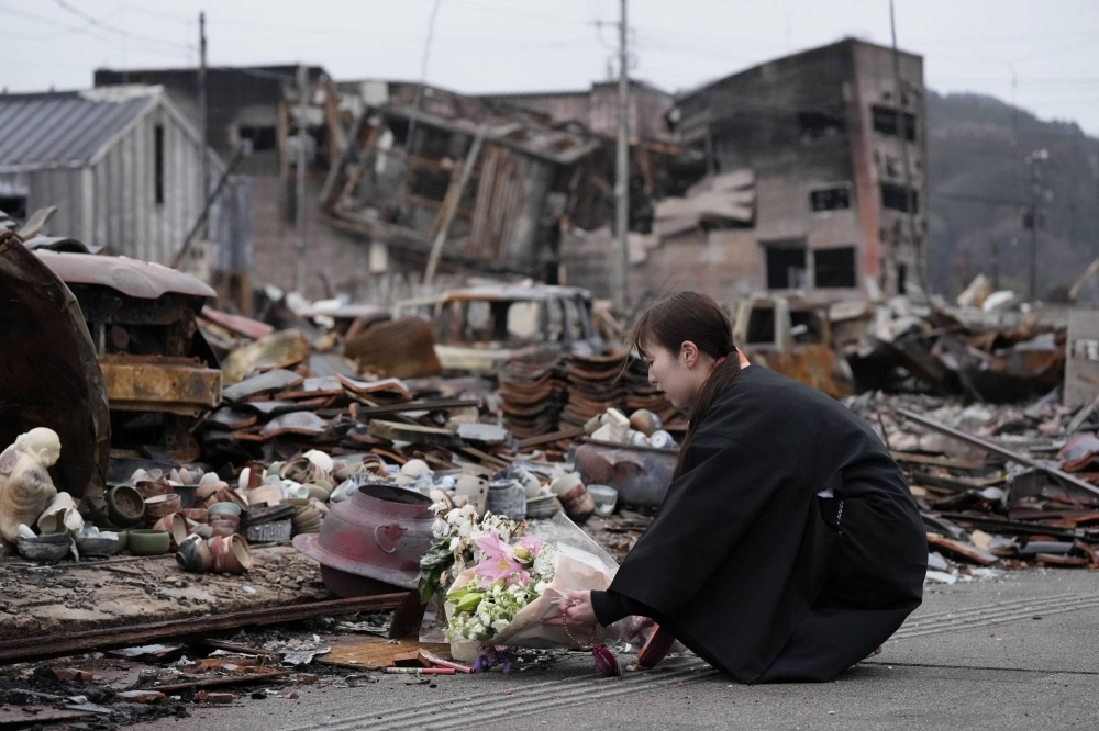 A woman offers flowers for victims of the New Year's Day earthquake near the morning market in the city of Wajima, Ishikawa Prefecture, on Thursday. Most buildings in the market were burned down in a fire that followed the quake.