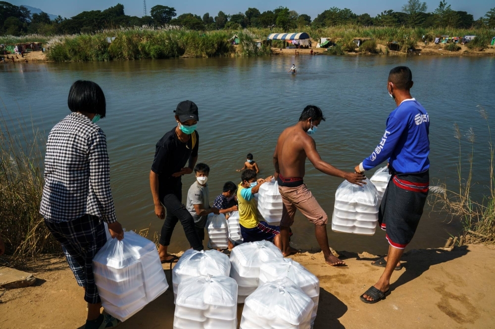 Refugees, who fled a flare-up in fighting between the Myanmar army and insurgent groups and settled temporarily on the Moei River bank, receive aid from Thailand on the Thai-Myanmar border, in Mae Sot, Thailand, in January 2022.