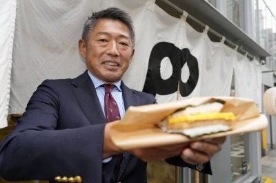 Katsuaki Kiyokawa, president of Potama Co., holds a pork and fried egg rice ball outside one of his stores in Fukuoka.