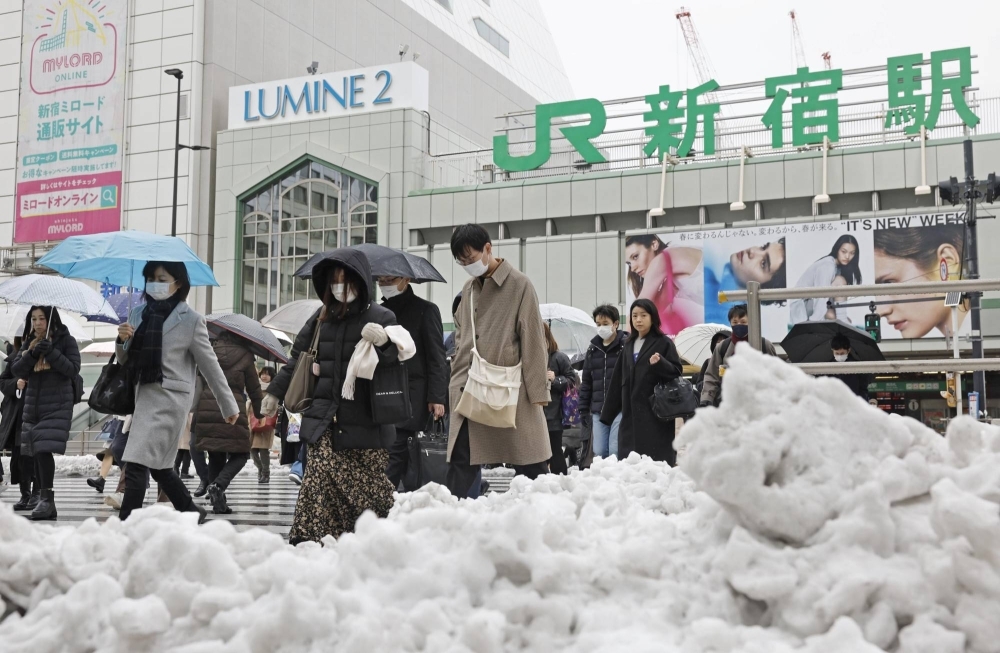 Commuters walk outside the Shinjuku Station Tuesday morning with snow still accumulated on walkways.  