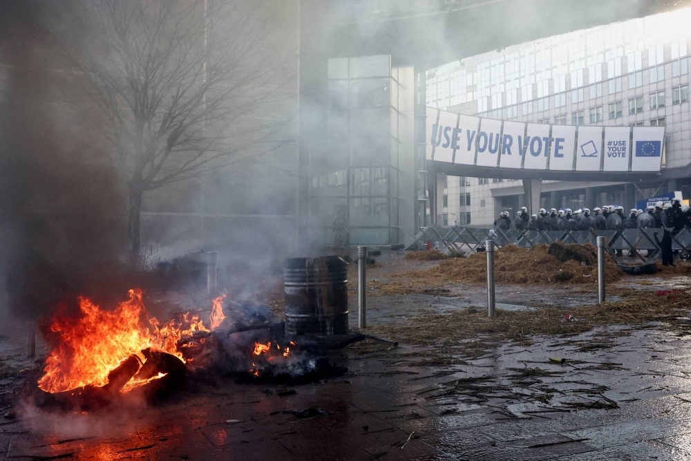 Police in riot gear stand guard next to a barricade near a fire outside the European Parliament in Brussels on Feb. 1 during a protest by farmers from Belgium and other EU countries over price pressures, taxes and green regulation.